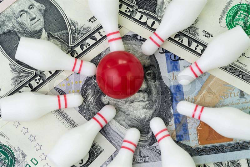 Red winning bowling strike ball surround with knocked down pins on pile of US dollar banknotes money, financial success target concept, goals on investment or profit ..., stock photo