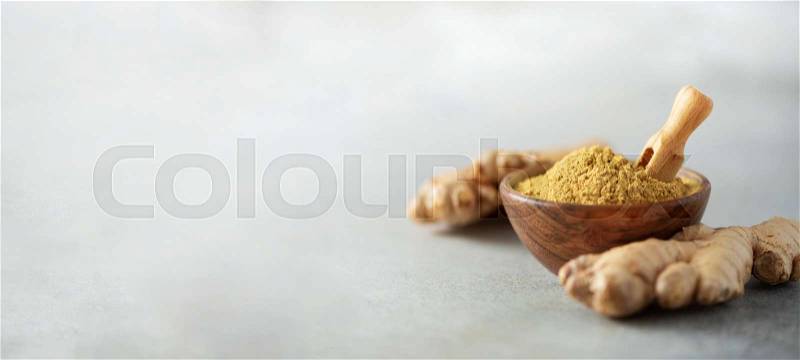 Ginger root and ginger powder in wooden bowl over grey concrete background with copy space. Immune system support. Ayurvedic treatment, stock photo