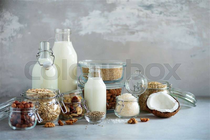 Glass bottles of vegan plant milk and almonds, nuts, coconut, hemp seed milk on grey concrete background. Banner with copy space. Dairy free milk substitute drinks ..., stock photo
