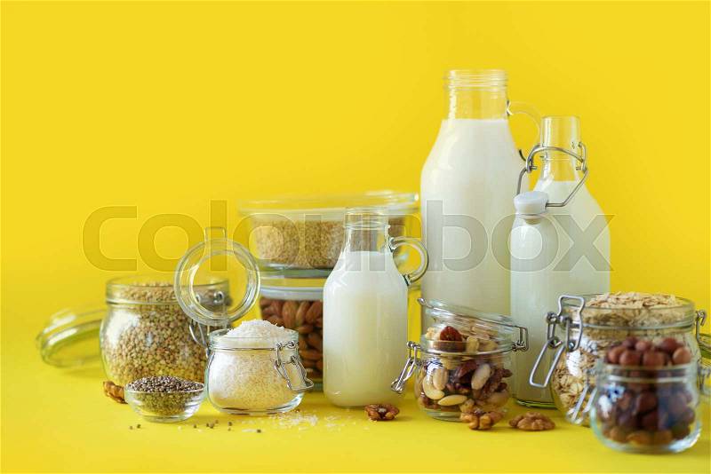 Glass bottles of vegan plant milk and almonds, nuts, coconut, hemp seed milk on yellow background. Banner with copy space. Dairy free milk substitute drinks and ..., stock photo