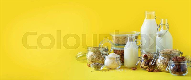 Glass bottles of vegan plant milk and almonds, nuts, coconut, hemp seed milk on yellow background. Banner with copy space. Dairy free milk substitute drinks and ..., stock photo