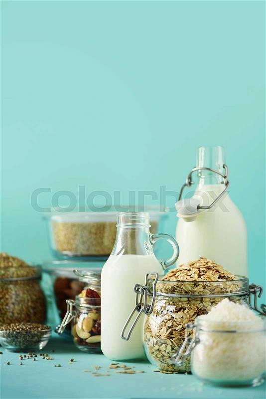 Glass bottles of vegan plant milk and almonds, nuts, coconut, hemp seed milk on blue background. Banner with copy space. Dairy free milk substitute drinks and ..., stock photo