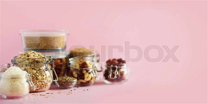 Grains, cereals, nut, dry fruits in glass jars over pink background with copy space. Clean eating, healthy, vegan diet concept, stock photo