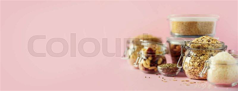 Vegan health food over pink background with copy space. Nuts, seeds, cereals, grains in glass jars. Antioxidants, omega 3, protein and dietary fiber concept, stock photo