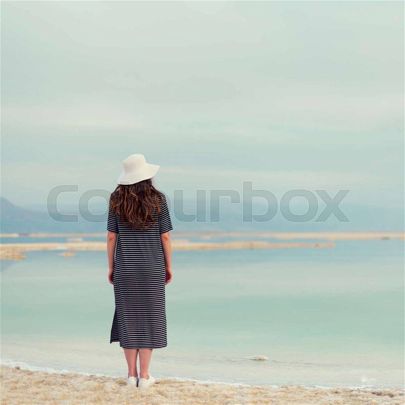 Woman in sailor striped dress near seaside of Dead Sea beach. Travel, summer vacation, holiday, freedom concept. Digital detox. Sea background with copy space. ..., stock photo