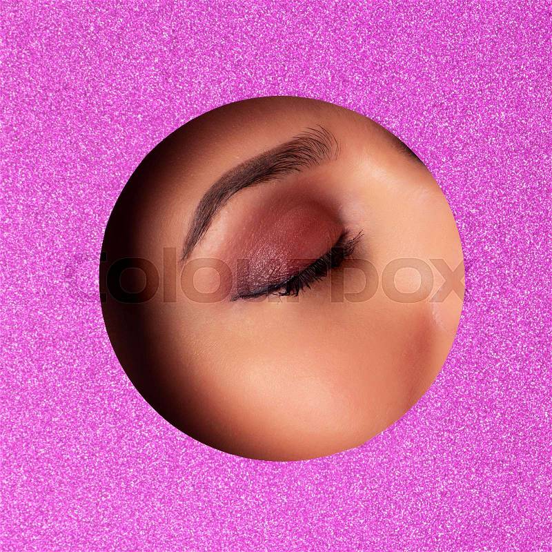 Girl with bright eyes make up looks through hole in violet paper. Business card of artist, beauty concept. Square crop. Cosmetics sale. Beauty salon advertising ..., stock photo