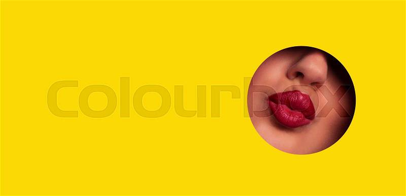 View of beautiful red lips giving kiss through hole in yellow paper background. Make up artist, beauty concept. Ready to new year party. Cosmetics sale. Beauty salon ..., stock photo
