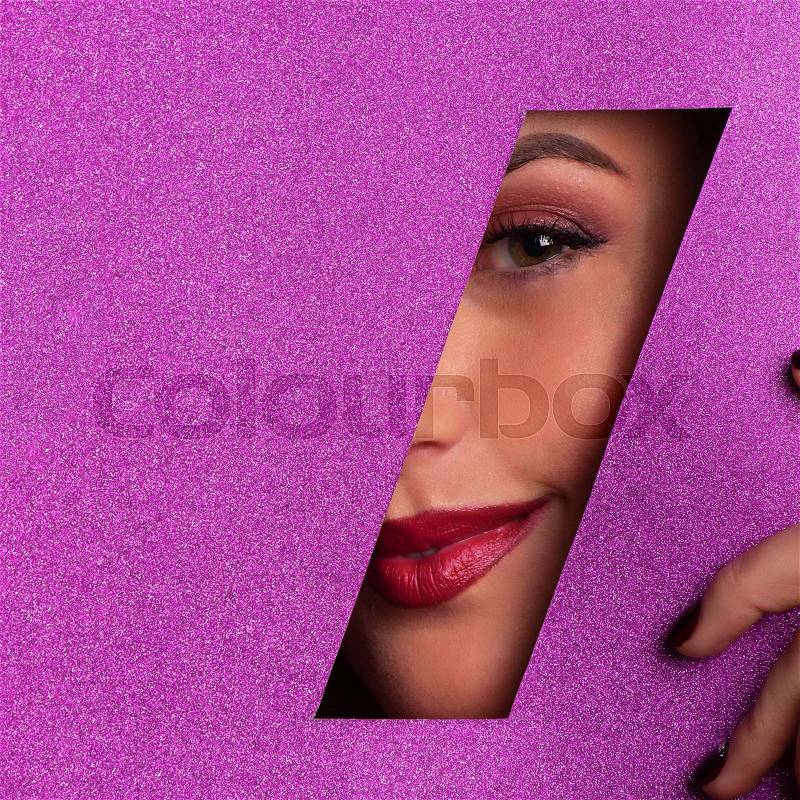 Girl with bright make up, red lipstick looking through hole in violet paper. Make up artist, beauty concept. Cosmetics sale. Square crop. Beauty salon advertising ..., stock photo