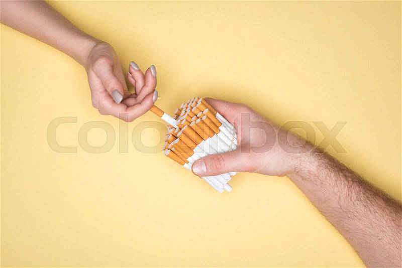 Cropped shot of woman and man holding cigarettes isolated on yellow, stock photo