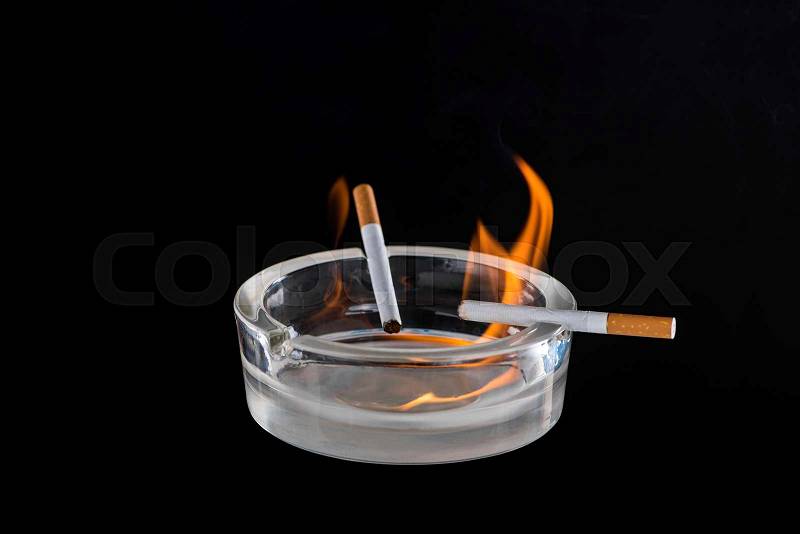 Studio view of glass ash-pot with burning cigarettes isolated on black, stock photo