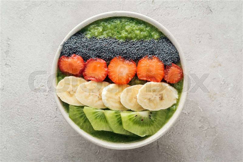 Top view of delicious smoothie bowl with fresh fruits on grey background, stock photo