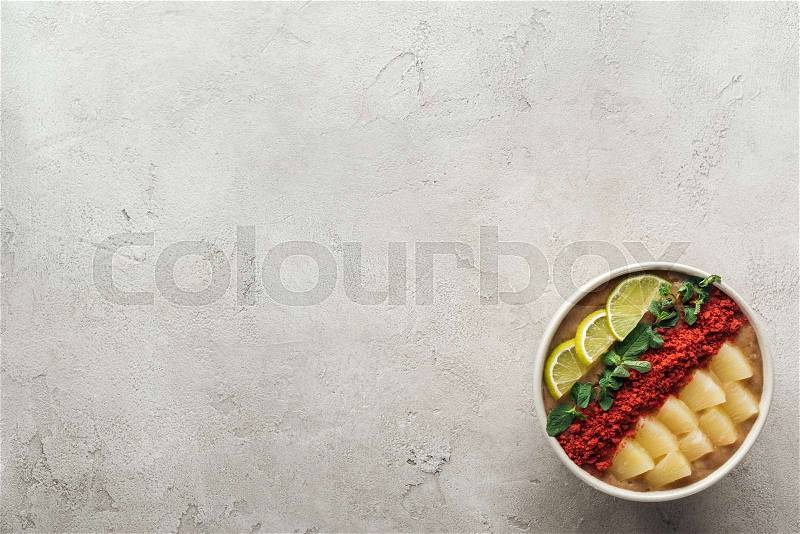 Top view of fresh smoothie bowl with lemons, mint and pineapples on grey background with copy space, stock photo