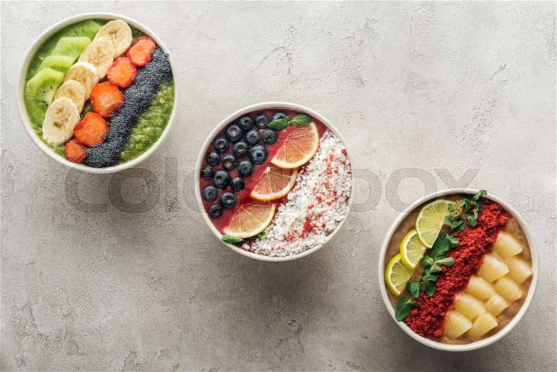 Top view of healthy organic smoothie bowls with fruits on grey background, stock photo