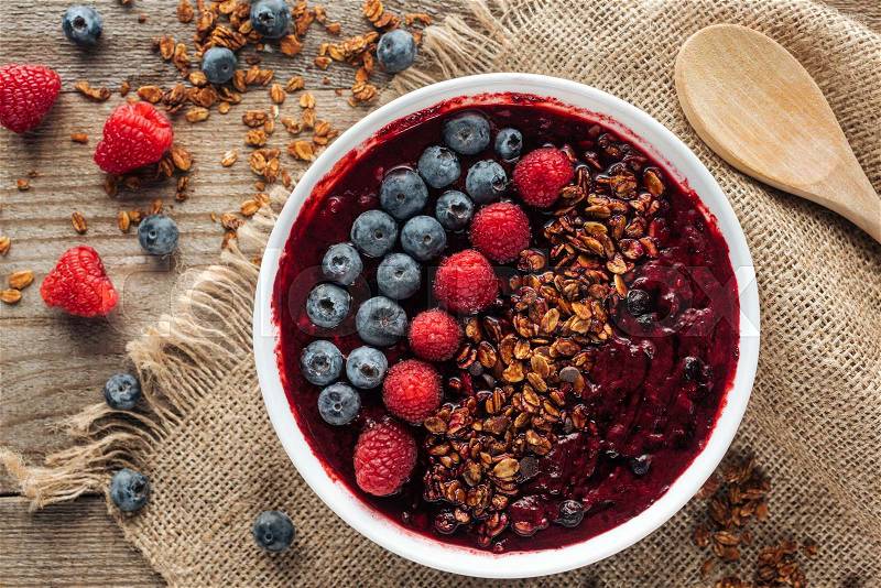Top view of delicious organic smoothie bowl with berries and granola on sackcloth, stock photo