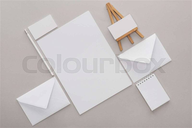 Flat lay with white empty papers and letters with toy easel at workplace on grey background, stock photo