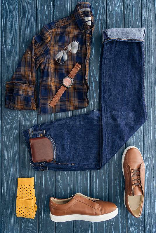 Flat lay with trendy checkered shirt, jeans and brown boots on wooden background, stock photo