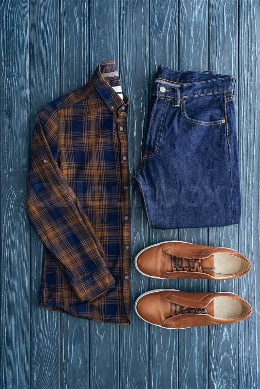 Top view of checkered shirt, jeans and brown shoes on wooden background, stock photo