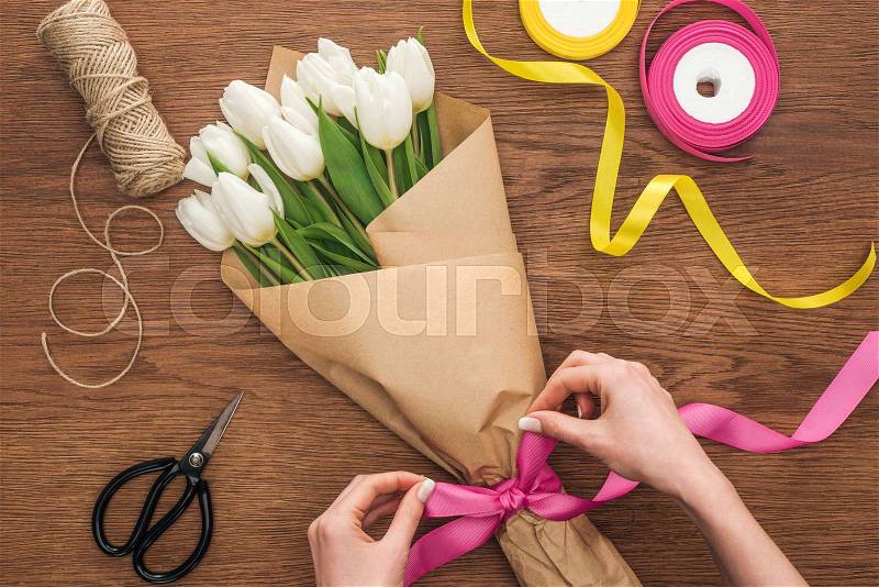 Partial view of on florist making bouquet of white tulips with ribbon on wooden background, stock photo