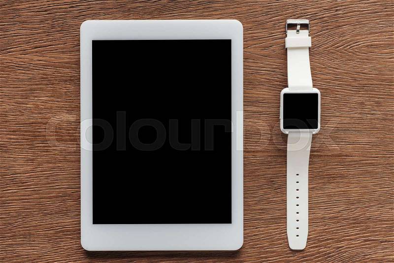 Top view of digital tablet and smartwatch with blank screen on wooden background, stock photo