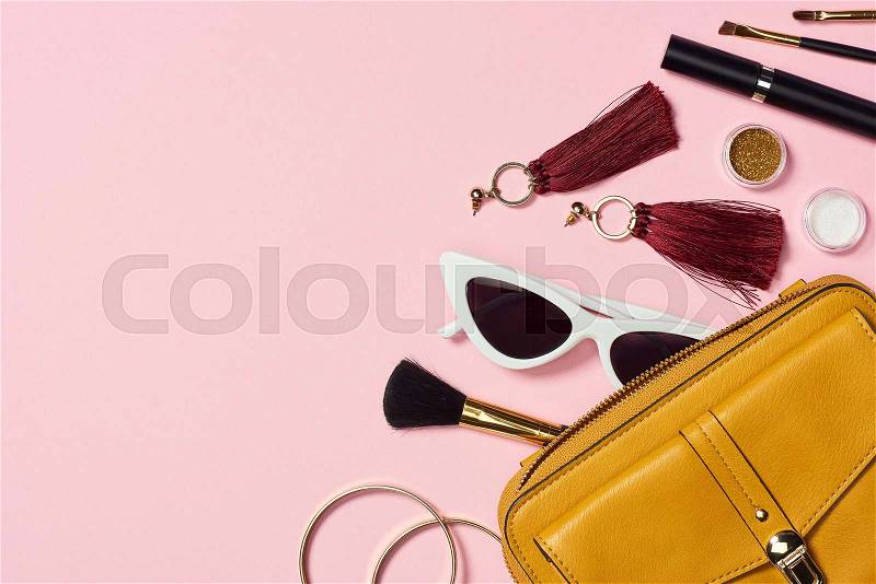Top view of bracelets, earrings, sunglasses, mascara, cosmetic brushes, eyeshadow and bag on pink background, stock photo