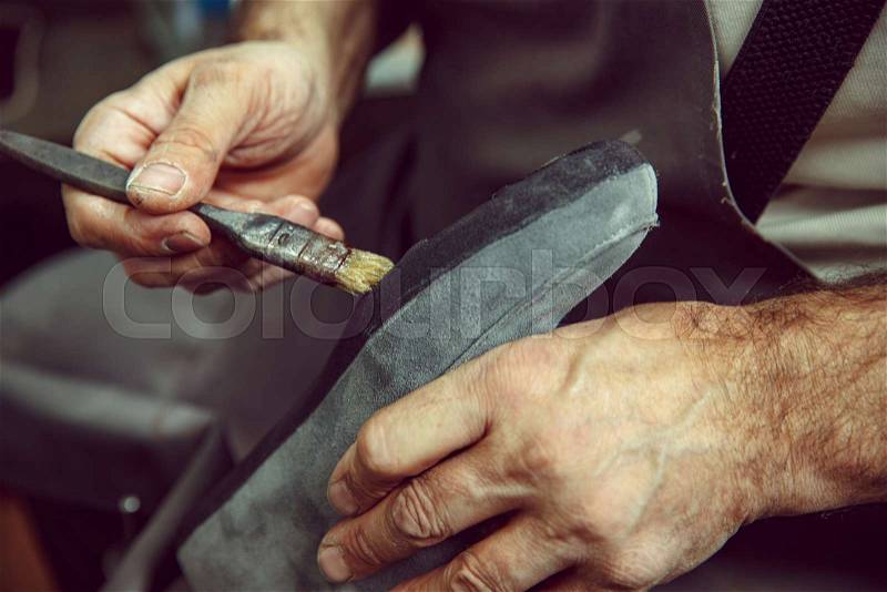 Shoemaker makes shoes for men. He smears special liquid with a brush. The man in female profession. Gender equality concept, stock photo