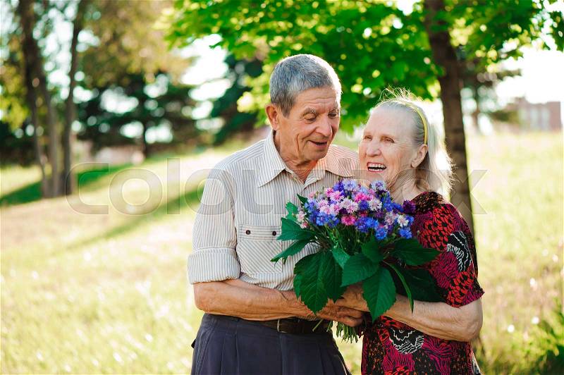 An elderly man of 80 years old gives flowers to his wife in a summer park, stock photo
