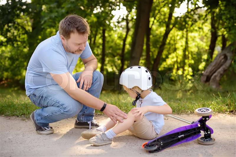 Little boy in safety helmet falls during learning to ride scooter. Father comforting his son after crash. Active family leisure. Child in helmet. Safety, sports, ..., stock photo