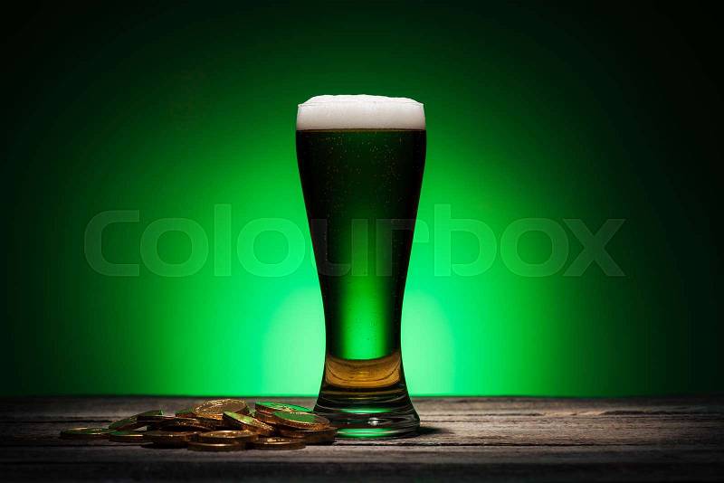 Glass of green beer near golden coins on st patricks day on green background, stock photo