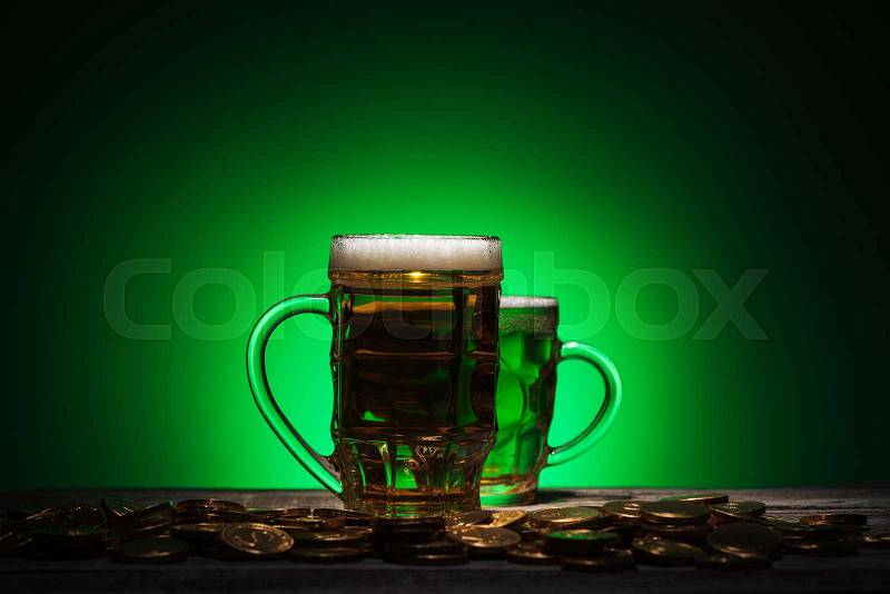 Glasses of irish beer standing near golden coins on green background, stock photo