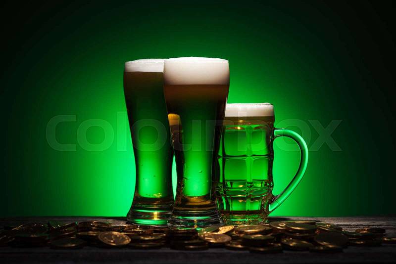 Glasses of irish beer standing near golden coins on table on green background, stock photo