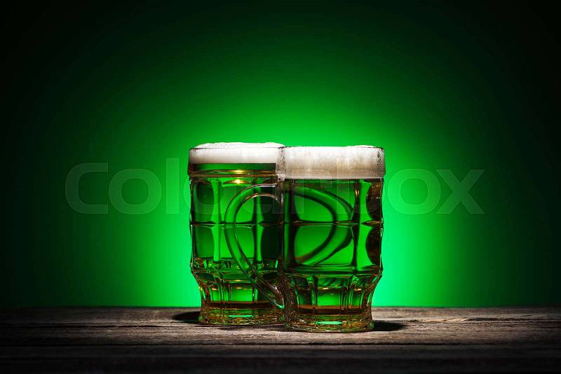 Glasses of irish beer standing on wooden table on green background, stock photo
