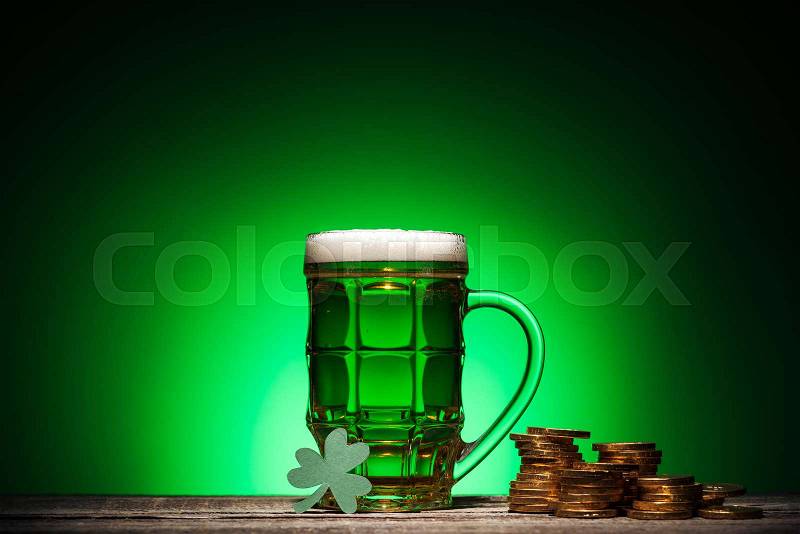 Glass of green irish beer near golden coins and cube calendar on green background, stock photo