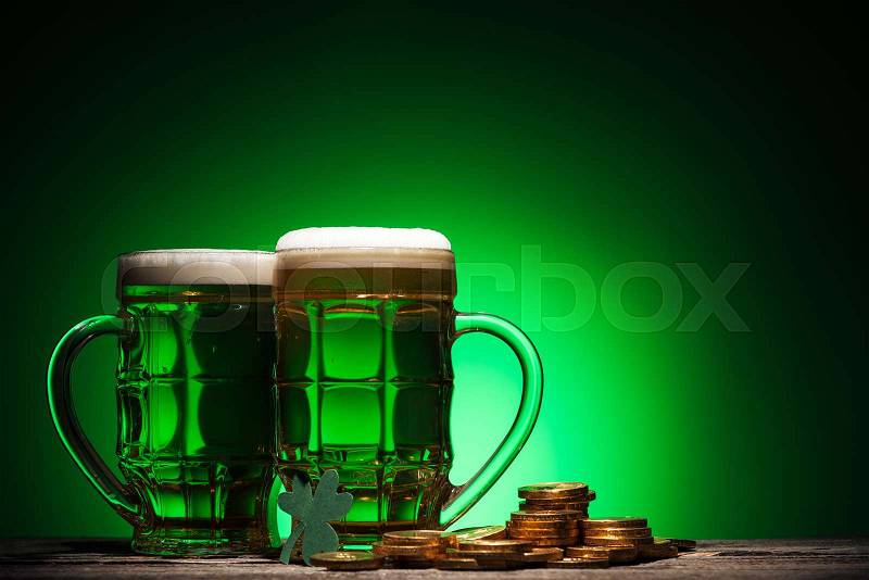 Glasses of irish beer near golden coins on st patricks day on green background, stock photo