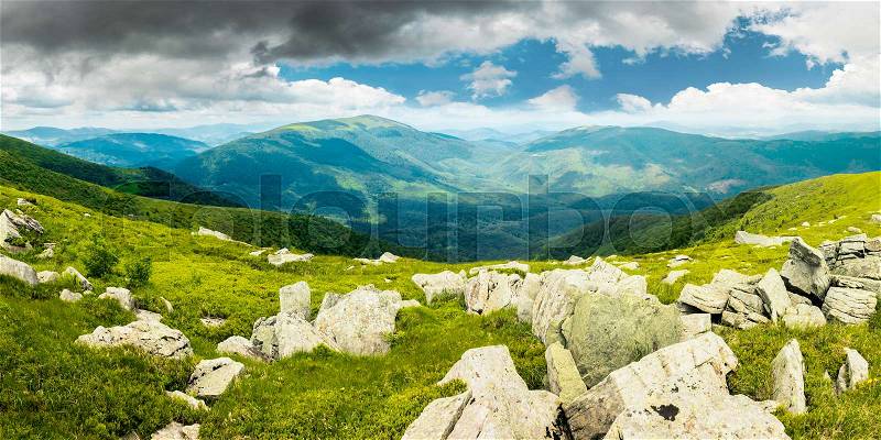 Panorama of mountain landscape in summer. rocks lay among on a grassy slope down to the valley. beautiful view. overcast cloudy sky. windy summer weather, stock photo