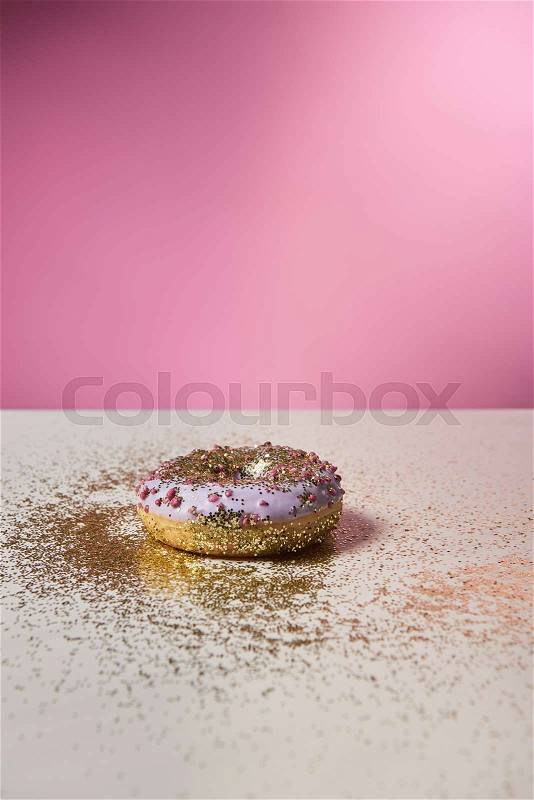 Glazed doughnut with shiny sparkles on white table on pink background, stock photo