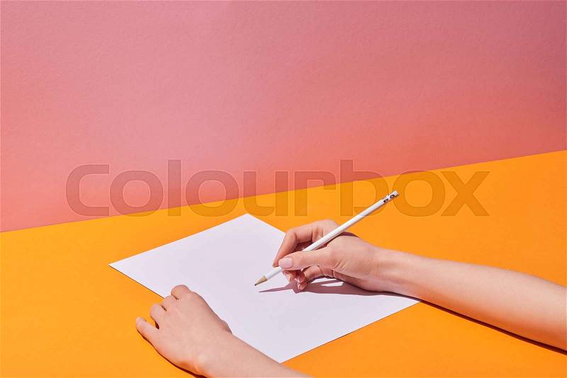 Cropped view of woman writing on paper sheet by pencil on yellow desk, stock photo