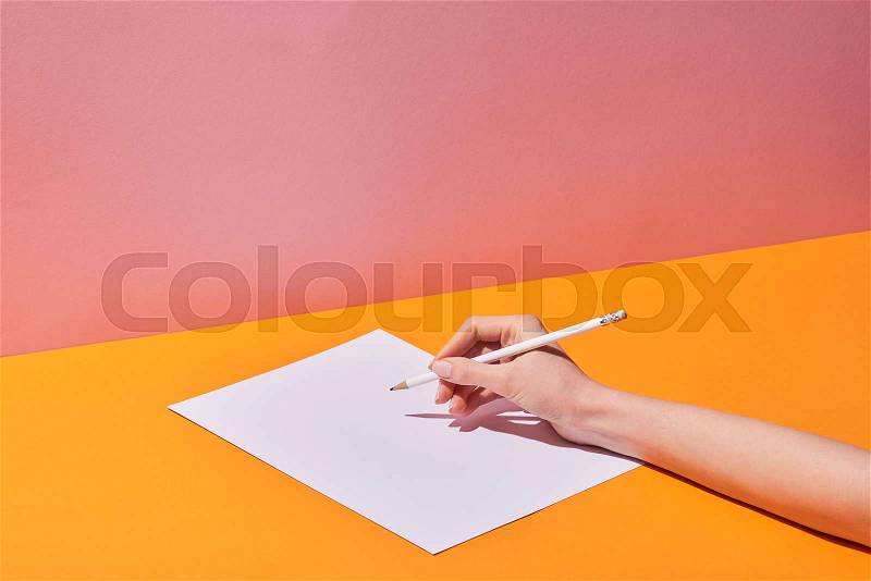 Cropped view of woman writing on paper on yellow desk and pink background, stock photo