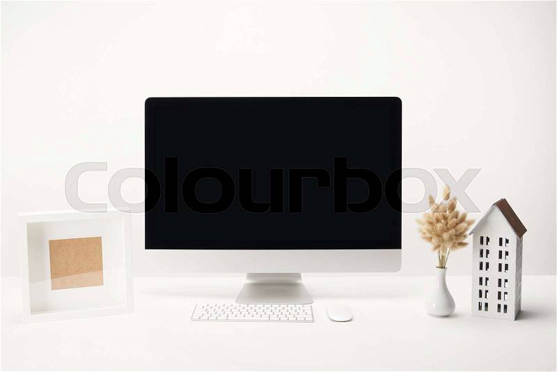 Workplace with house model, dry flowers, photo frame and desktop computer with copy space isolated on white, stock photo