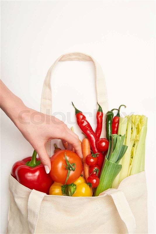 Partial view of woman taking out tomato of bag with vegetables on white background, stock photo