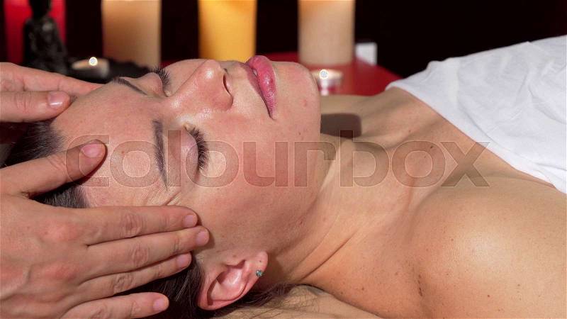 Lovely young woman enjoying face massage with her eyes closed. Cropped shot of a woman resting at spa center, during head massage. Skincare, rejuvenation, ..., stock photo