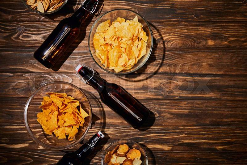 Top view of party snacks in bowls near brown bottles with beer on wooden table, stock photo