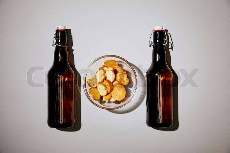 Top view of brown bottles with beer near snack in bowl on white background, stock photo