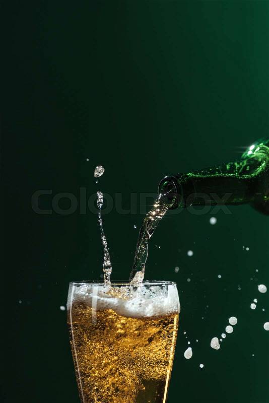 Pouring beer into glass with splashes and copy space isolated on green, st patrick day concept, stock photo