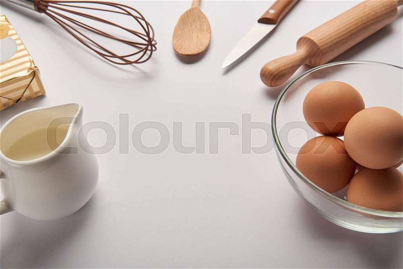 Close up of cooking utensils, butter, jar with milk and eggs in bowl on grey surface, stock photo