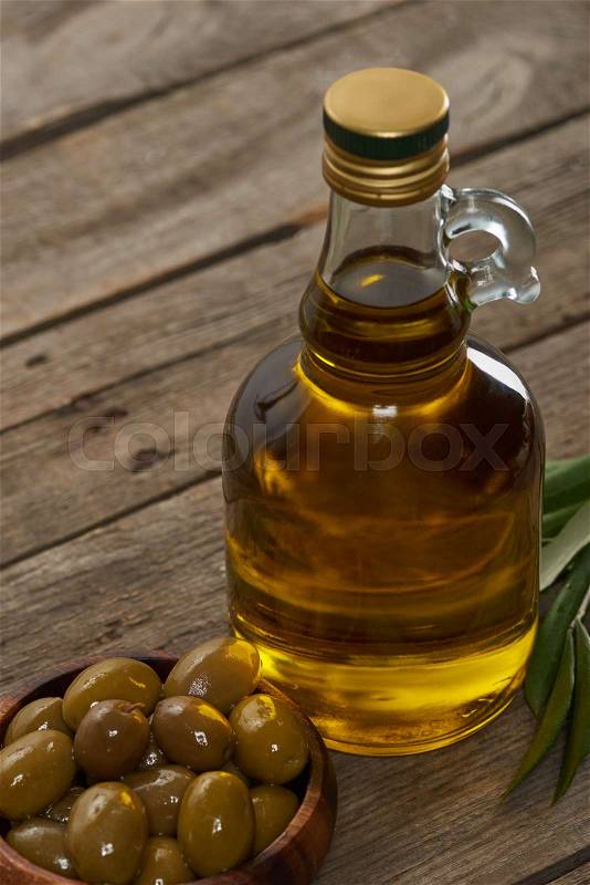 Oil bottle, bowl of olives and olive tree leaves on wooden surface , stock photo