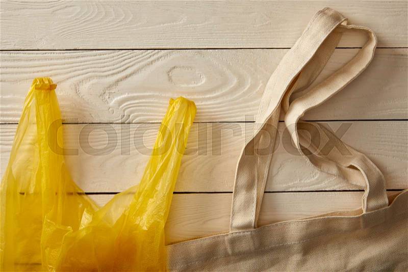 Top view of cotton string bag and plastic bag on white wooden surface, zero waste concept, stock photo