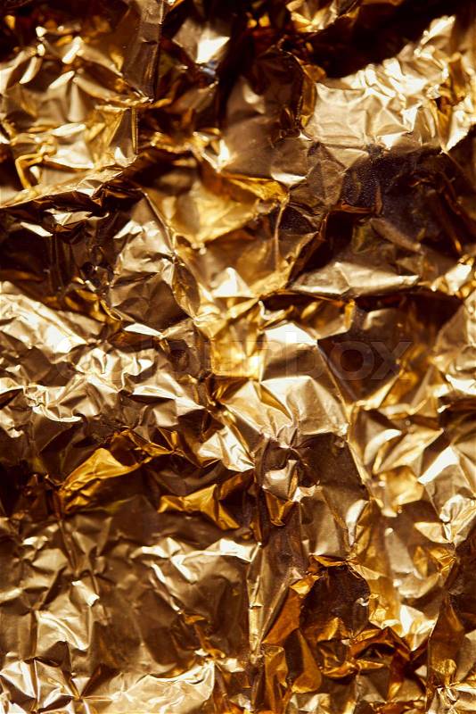 Crumpled golden foil sheet with bright twinkles and shadows, stock photo