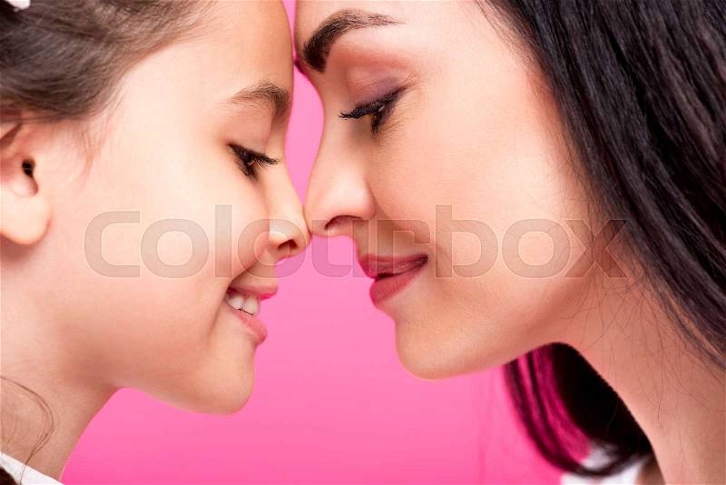 Side view of beautiful happy mother and daughter touching foreheads isolated on pink, stock photo