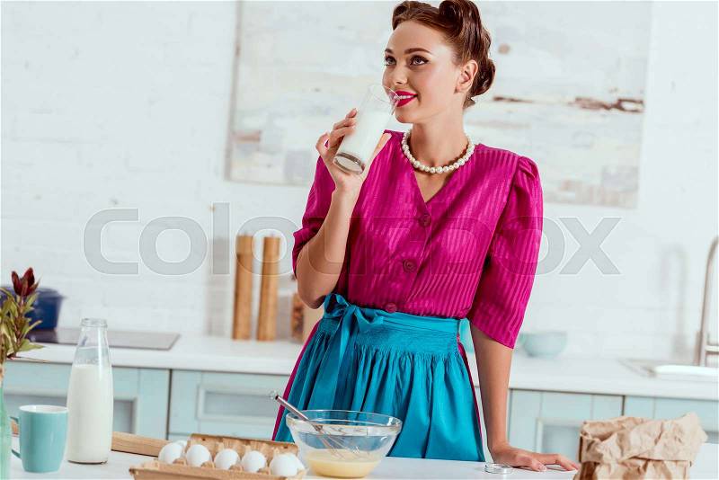 Elegant pin up girl drinking milk standing near kitchen table with different products, stock photo