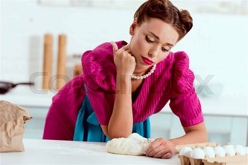 Tired pin up girl with flour leaning on kitchen table, stock photo